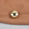 Detailed macro view showing the polished mirror finish of a round gold metallic brooch - Gold