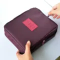 Large capacity waterproof travel makeup storage bag in deep burgundy held by hands - Burgundy