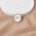 Primer plano de broche magnético ovalado con borde de perlas y lazo dorado. - Blanco con Lazo