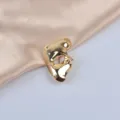 Detailed view of a vintage golden mask-shaped brooch on champagne satin fabric. - Gold