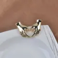Detailed view of a shiny gold heart hands brooch on a white decorative ceramic plate. - Heart Hands Style / Gold