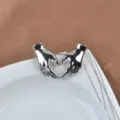 Detailed macro view of a silver heart-shaped hands brooch on a white decorative ceramic plate - Heart Hands Style / Silver