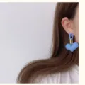 Primer plano de un pendiente de corazón azul mate con detalles de eslabones dorados. - Azul zafiro