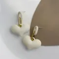 Makroansicht von eleganten cremefarbenen matten Herzohrringen mit goldenen Metallgliedern - Weiß