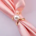 Detailed close-up of a elegant golden scarf ring with a central pearl on pink silk. - Model 01 Gold