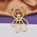 Detailed macro view of a golden hollow bear brooch with black bead eyes and tiny bow - Gold