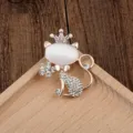 Detailansicht einer goldenen Katzenbrosche mit weißem Opal und funkelnder Kristallkrone. - Krone Katze Stil (05)