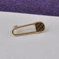 Detaillierte Nahaufnahme einer goldenen Sicherheitsnadel-Brosche mit "FOREVER"-Gravur. - FOREVER Gravurstil