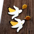 Detailansicht der verspielten Acryl-Bananenohrringe auf dunkler Holzoberfläche. - Banane