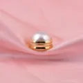 Close-up detail of a premium white pearl magnetic brooch pin displayed on pink satin fabric - White