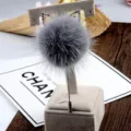 Macro view of a grey faux fur pom-pom brooch pin with sparkling rhinestone cat ears decoration. - Gray