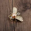Detailaufnahme einer goldenen Bienenbrosche mit rosa Perle und Glitzersteinen - Vergoldet Goldperle
