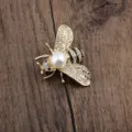 Nahaufnahme einer goldenen Bienennadel mit funkelnden Kristallen und Perlendetail - Vergoldet Weiß Perle