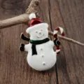Detailansicht einer Emaille-Schneemann-Brosche mit Zuckerstange auf rustikalem Holzhintergrund - Schneemann