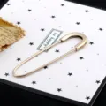Close-up of a large gold-toned safety pin brooch displayed on a star-patterned card - Gold