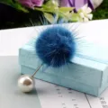 Detailansicht einer blauen Nerzpelz-Brosche mit weißer Perle auf einer blauen Geschenkbox. - Nerzfell-Perlenbrosche (746) / Pfauenblau