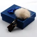 Detailansicht einer flauschigen Nerzfell-Brosche mit braunen Wildleder-Quasten auf blauer Box - Champagner