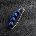 Nahaufnahme einer eleganten goldfarbenen Sicherheitsnadel mit tiefblauen Perlen. - Blau