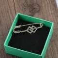 Detailansicht einer goldfarbenen Brosche mit geometrischen Strasssteinen in grüner Box. - Doppelquadrate
