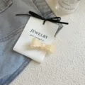 Elegante cremefarbene Haarspange mit Schleife auf einer weißen Karte auf hellem Denim-Stoff. - Spitzenkante-Stil / Milchweiß