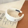 Elegante diadema ancha de lana blanco crema con un sofisticado logo ovalado dorado - Blanco
