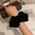 Macro view of a soft black velvet scrunchie worn on a wrist for elegant styling - Velvet Style / Black