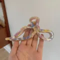Detailed view of a colorful marble acetate bow hair claw clip held against a plain wall - Purple Yellow Gradient