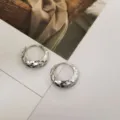 Vista de detalle de pendientes de aro de plata S925 con textura de estrella facetada - Oro blanco