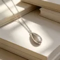 Collar minimalista de plata S925 con colgante de gota sobre fondo de libro beige - Oro blanco