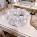Gedetailleerd overzicht van de prachtige witte satijnen sieradenschaal met strik op tafel. - Bloemblaadje / Wit