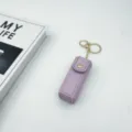 Close up detail view of a stylish purple leather lipstick case keychain with gold tone hardware. - Purple