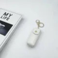 White leather lipstick case keychain detail view, portable makeup holder with gold hardware. - White