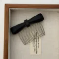High-definition close-up of a minimalist matte black bow hair comb with silver teeth. - Black