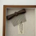 Detailed close-up of a brown matte bow hair comb presented in a rustic wooden jewelry tray - Chocolate