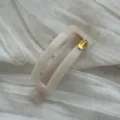 Detailansicht einer eleganten cremefarbenen ovalen Haarklammer mit goldenem Hand Made Tag - Hohles Quadrat / Gelee-Weiß
