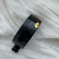 Nahaufnahme einer glänzend schwarzen ovalen Haarspange mit goldenem Etikett. - Quadratisch / Hellschwarz