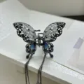 Detailed view of a metal butterfly hair claw clip with blue crystals and long tassels. - Black