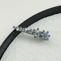 Close-up detail of an elegant floral crystal hair clip resting on a white woven background. - Blue