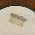 Detailansicht eines eleganten Kristall-Haarkamms mit goldfarbenen Metallzinken auf Textur - Hellviolett