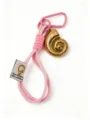 Detail view of the gold ammonite shell pendant and pink woven lanyard keychain accessory. - Pink