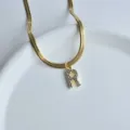 Gold flat snake chain necklace with sparkling crystal letter R pendant detail close up. - Letter R
