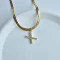 Detailed view of gold herringbone chain necklace featuring a sparkling zirconia pendant. - Letter X