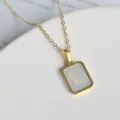 Nahaufnahme einer goldenen Halskette mit einem quadratischen Perlmutt-Buchstaben-Anhänger. - Buchstabe L