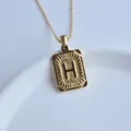 Close-up of gold rectangular initial pendant necklace with letter H detail on white dish. - Letter H Square Pendant / Gold
