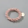 Close-up detail of a handmade pink crystal beaded hair ring with a gold engraved charm tag - Pink