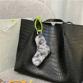 Detailed view of a soft leopard print plush sock charm hanging on a black crocodile tote bag - Grey Leopard Print