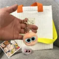 Detailed view of a cute plush pom-pom keychain with blue sunglasses and pearl charm. - Single OPP Bag Packaging / Pink