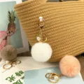 Close-up of soft pompom keychains with pearls and gold clips for bag decor. - White