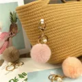 Detailed view of soft plush pompom keychain with pearl charm on a stylish straw bag - Dusky Pink