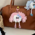 Detail view of a cute fuzzy pink curly hair plush doll keychain on a brown handbag - Pink